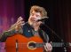 Mac McAnally talking on stage with guitar in hand