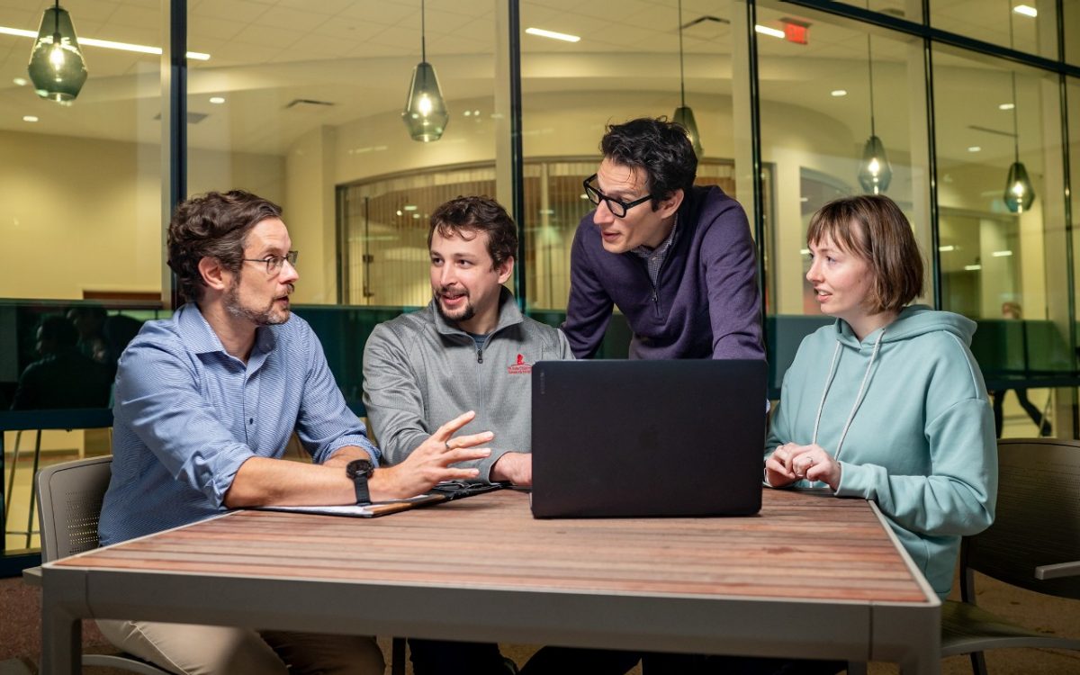 Group of St. Jude researchers discussing at table with open laptop